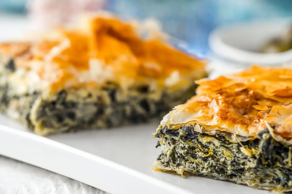 Two slices of spinach and feta pie with flaky golden filo on a white plate